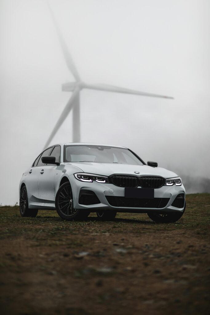 pexels-photo-12086412-12086412 A modern BMW car parked in a foggy landscape with a wind turbine in the background, capturing a blend of technology and nature.